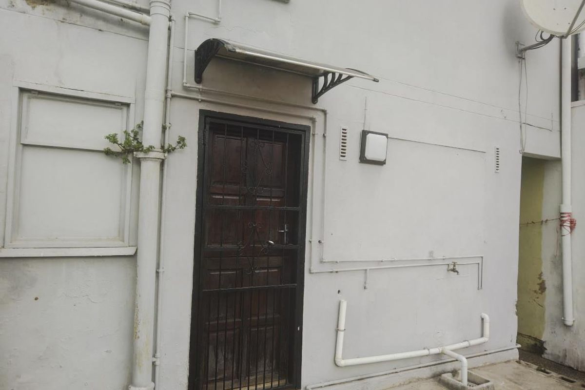 Rear exterior view showing a security door, external plumbing, and wall-mounted fixtures on a weathered facade.