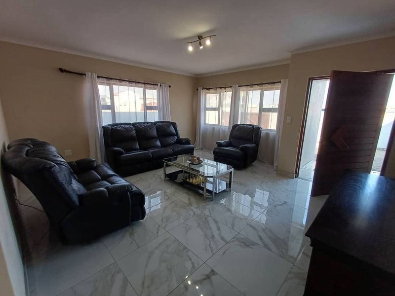 A bright living room featuring large windows, modern marble-look floor tiles, and a solid timber entrance door.