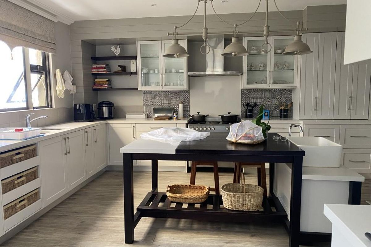 A well-appointed kitchen featuring shaker-style cabinetry, a central island with a farmhouse sink, stone countertops, and a built-in gas hob with extractor fan.
