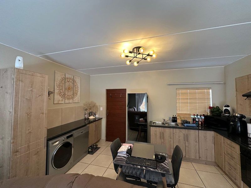Functional kitchen featuring light wood-finish cabinetry, dark granite countertops, double basin sink, and tiled flooring with integrated laundry appliance space.