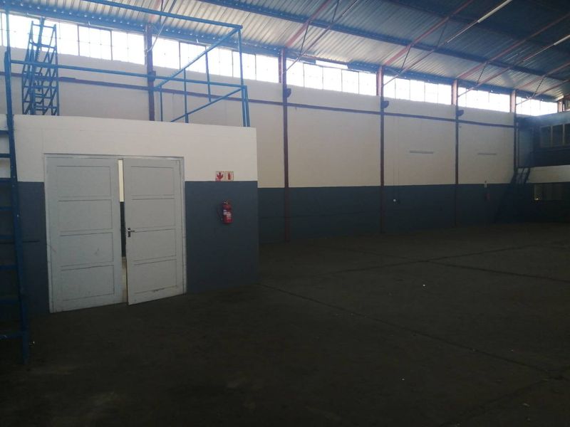 Spacious industrial warehouse unit featuring high ceilings with exposed steel trusses, clerestory windows for natural light, and concrete flooring.