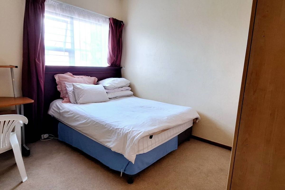 A functional bedroom featuring carpeted flooring, a window with curtain tracks, and built-in storage space.