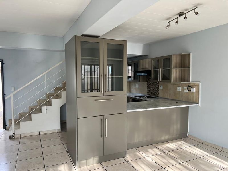 Open-plan kitchen area featuring modern cabinetry, marble-look countertops, and a built-in hob, adjacent to a staircase with a metal railing.