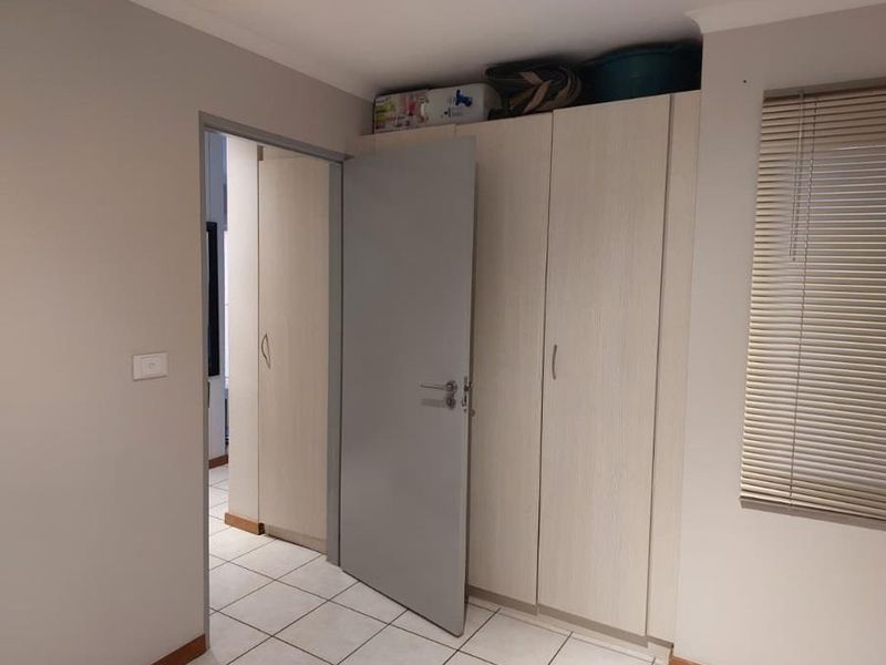 A clean bedroom featuring built-in cupboards, tiled flooring, and venetian blinds, offering a neutral and functional space.
