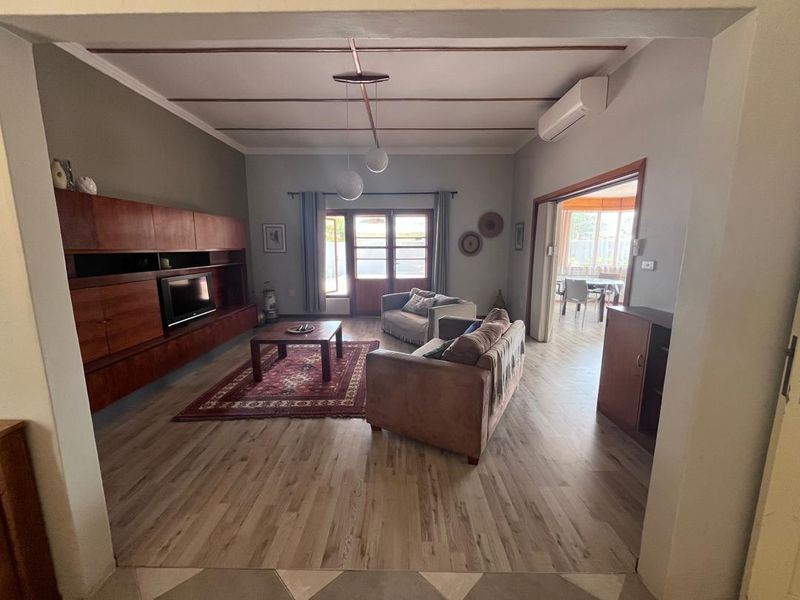 Spacious living room featuring laminate flooring, built-in cabinetry, and an air conditioning unit, with direct access to an adjoining sunroom.