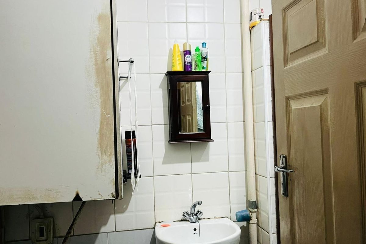 A compact bathroom featuring a pedestal sink, wall-mounted medicine cabinet, and white ceramic tiling with exposed plumbing fixtures.