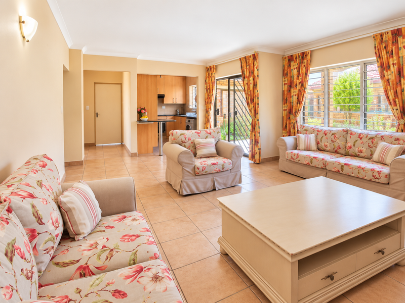 Spacious open-plan living area featuring tiled floors, integrated kitchen cabinetry, and large windows providing natural light with access to an outdoor patio area.