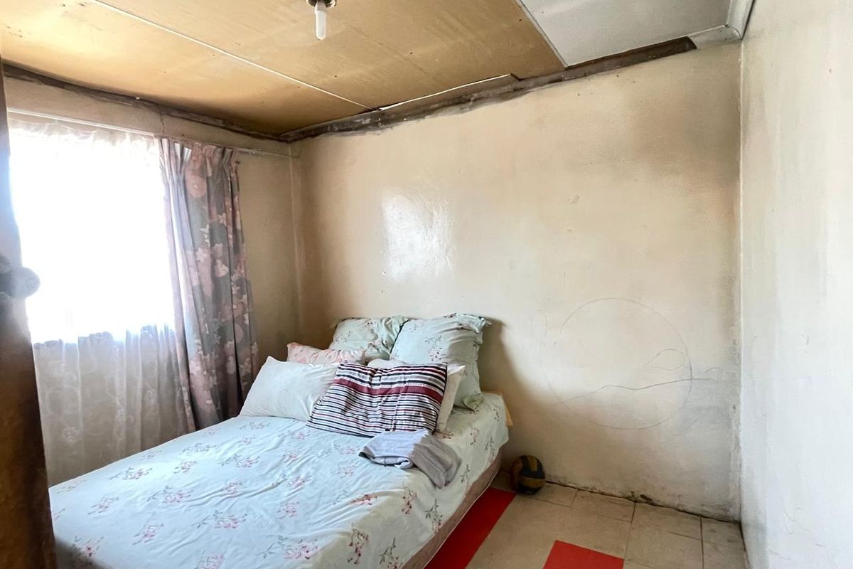 A bedroom featuring tiled flooring and a basic ceiling finish, requiring cosmetic updates and repairs to the wall and ceiling surfaces.