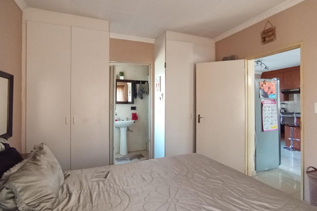 Bedroom featuring built-in cupboards, with an en-suite bathroom and a view through to the kitchen area.