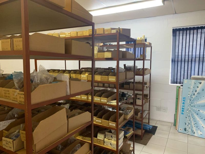 A functional utility or storage space featuring tiled flooring, fluorescent lighting, and vertical window blinds, currently utilized for organized inventory storage.