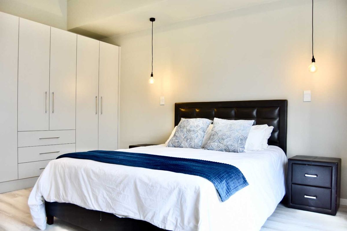 A well-maintained bedroom featuring built-in floor-to-ceiling wardrobes, modern pendant lighting, and neutral finishes.