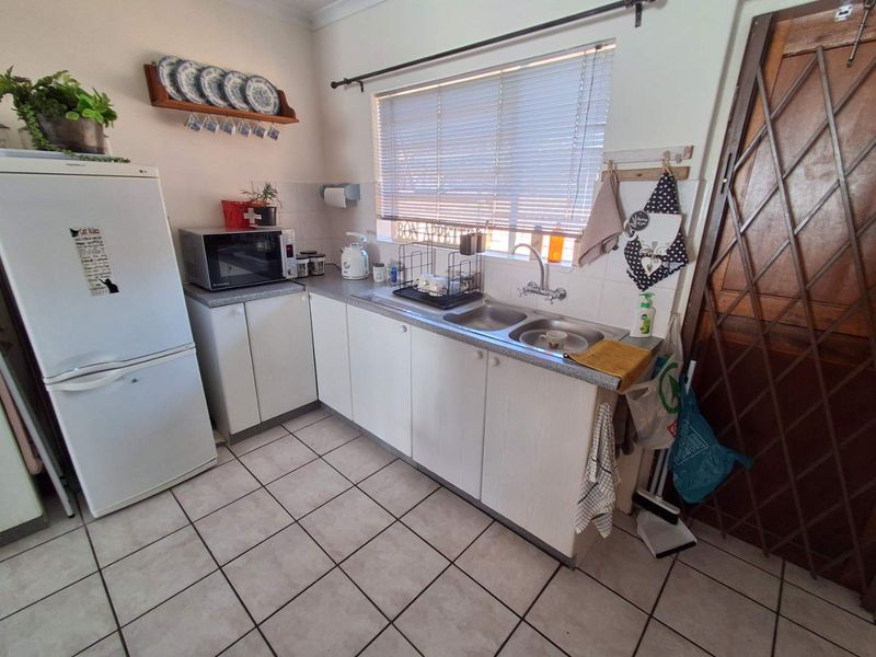 A functional kitchen featuring white laminate cabinetry, a double bowl stainless steel sink, tiled flooring, and a window with venetian blinds.