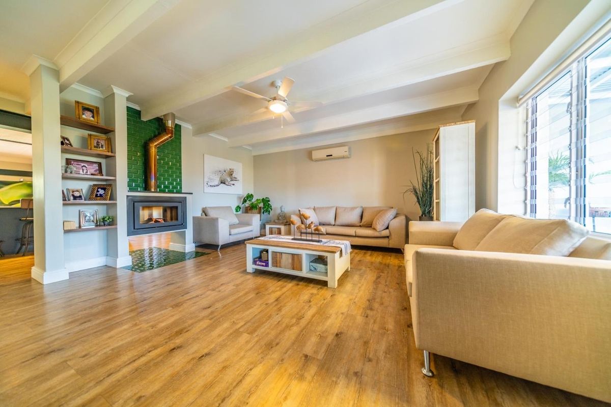 Spacious living room featuring wood-look flooring, exposed ceiling beams, a built-in fireplace with green tile surround, and a wall-mounted air conditioning unit.