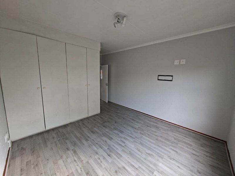 A vacant bedroom featuring light-toned laminate flooring, built-in cupboards, and a wall-mounted TV bracket, offering a clean and neutral space.