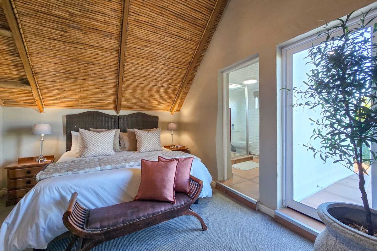 A cozy bedroom featuring a vaulted bamboo ceiling, carpeted flooring, and an en-suite bathroom with a glass-enclosed shower.