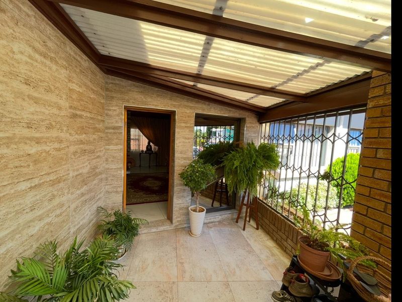 A covered patio area featuring travertine wall cladding, tiled flooring, and a corrugated roof, providing a sheltered outdoor space.