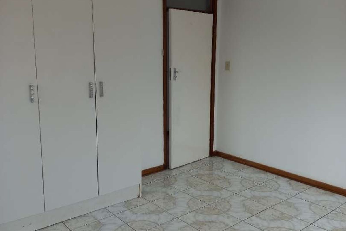 A simple bedroom featuring built-in cupboards and tiled flooring, offering a clean and functional space.