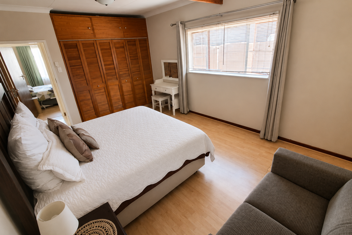 A well-maintained bedroom featuring laminate flooring, built-in wooden cupboards, and an exposed ceiling beam, offering a comfortable and functional living space.