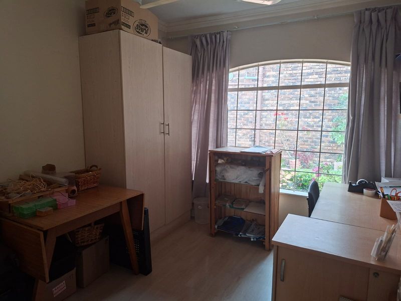 A functional bedroom featuring a built-in wardrobe, laminate flooring, and an arched window with security bars overlooking the garden.