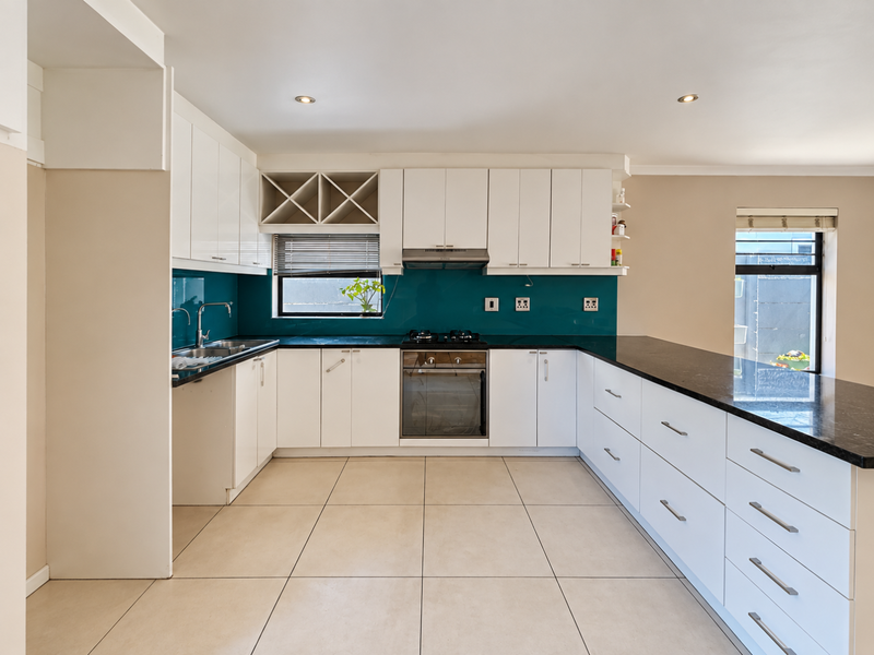 Modern kitchen featuring white cabinetry, dark granite countertops, a vibrant glass splashback, built-in oven, gas hob, and tiled flooring.