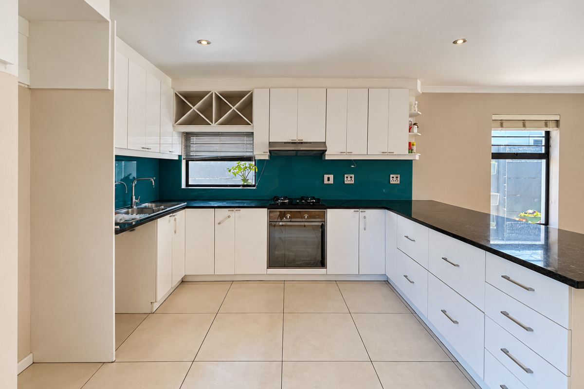 Modern kitchen featuring white cabinetry, dark granite countertops, a vibrant glass splashback, built-in oven, gas hob, and tiled flooring.