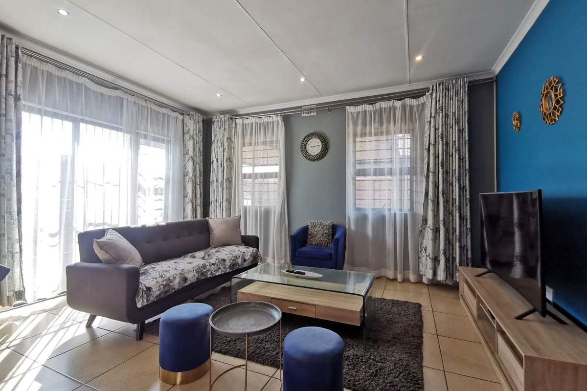 A bright and well-maintained living room featuring tiled flooring, recessed downlighting, and a large sliding glass door providing ample natural light.