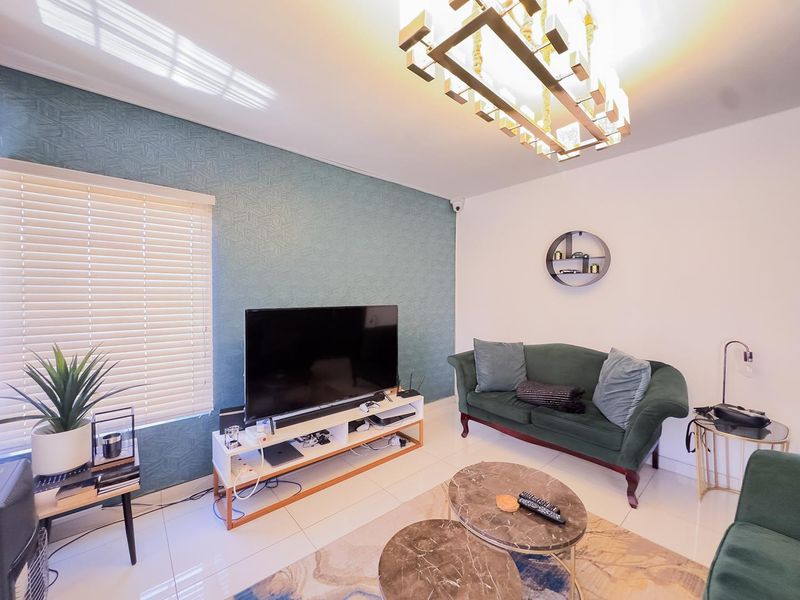 A well-maintained living room featuring a textured accent wall, tiled flooring, modern lighting, and venetian blinds, creating a comfortable and contemporary living space.