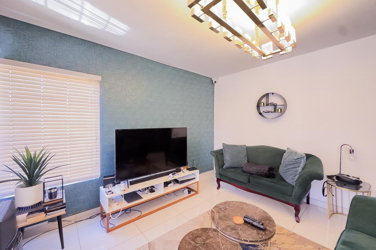 A well-maintained living room featuring a textured accent wall, tiled flooring, modern lighting, and venetian blinds, creating a comfortable and contemporary living space.