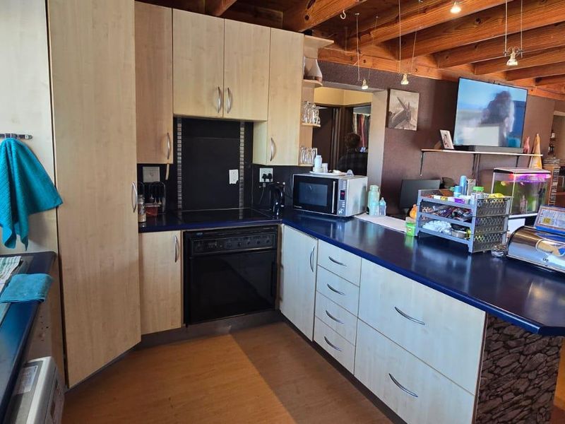 Open-plan kitchen featuring light wood cabinetry, blue laminate countertops, and exposed timber ceiling beams, seamlessly flowing into the adjacent living area.