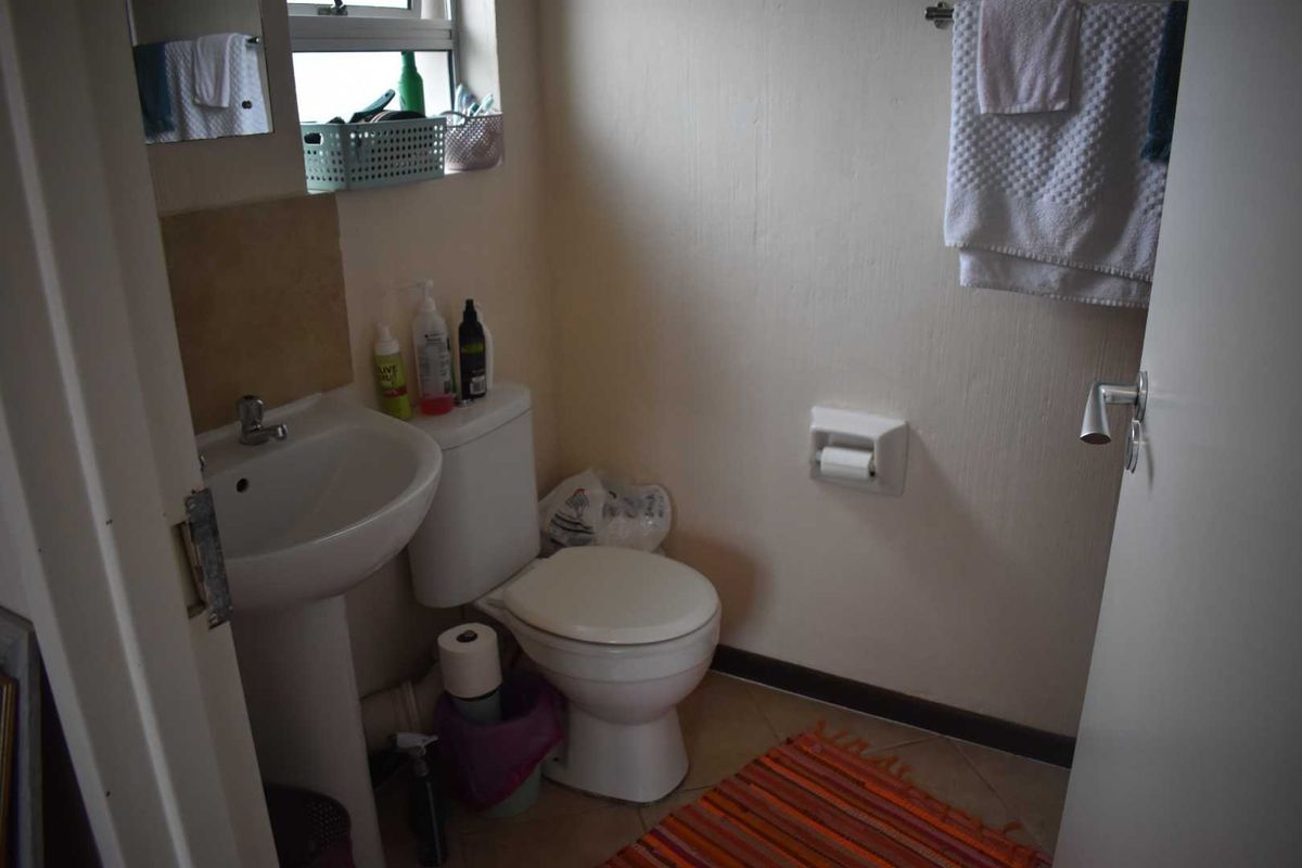 A compact bathroom featuring a pedestal basin, a standard toilet, and a small window, providing essential functionality in a modest space.