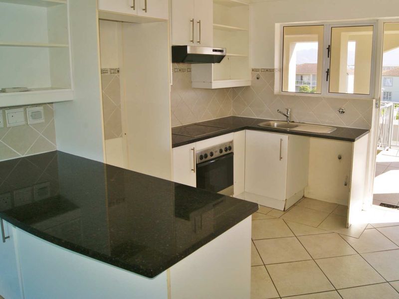 A functional kitchen featuring granite countertops, built-in oven, hob, and extractor fan, with direct access to an outdoor balcony area.