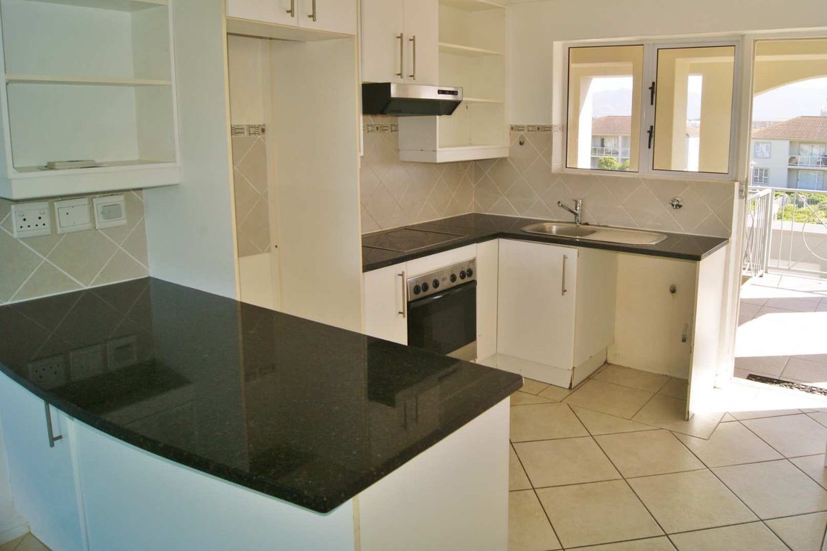 A functional kitchen featuring granite countertops, built-in oven, hob, and extractor fan, with direct access to an outdoor balcony area.