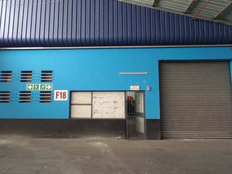 Industrial utility space featuring high-clearance metal roofing, multiple roller shutter doors, and integrated fire safety equipment within a functional warehouse environment.