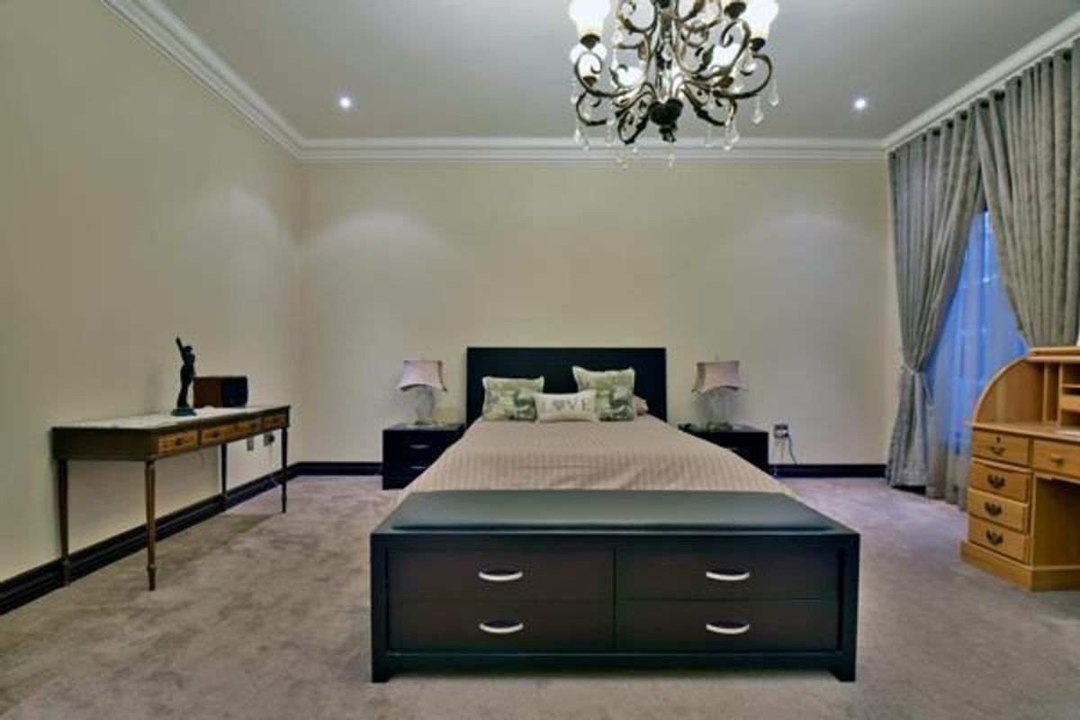 Spacious bedroom featuring crown molding, recessed lighting, and a decorative chandelier, finished with neutral wall tones and plush carpeting.