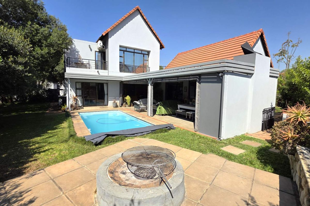 Rear exterior view featuring a swimming pool, covered patio area, and a built-in fire pit set within a landscaped garden.