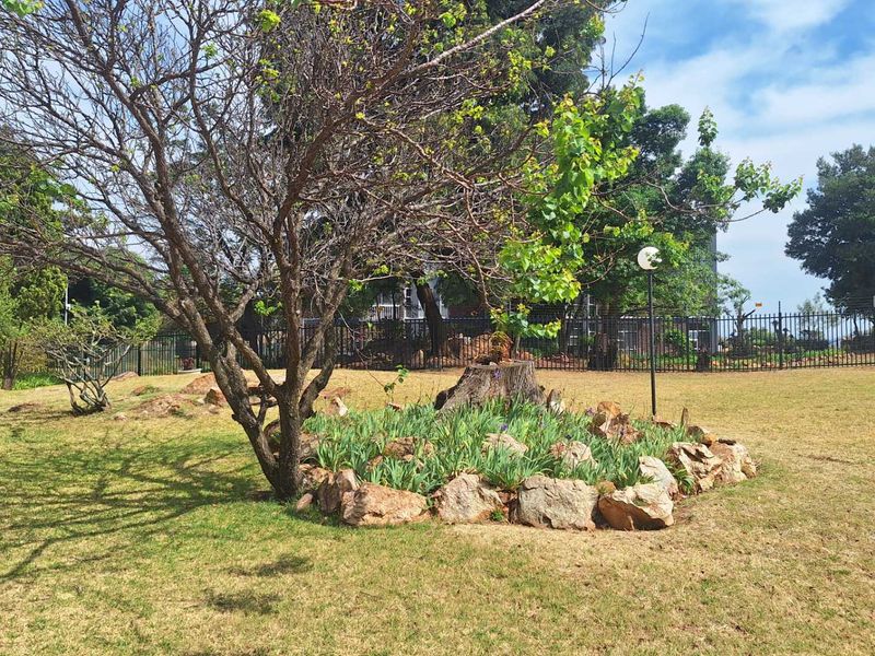 A well-maintained garden area featuring a landscaped rock-bordered bed, mature trees, and secure perimeter fencing.