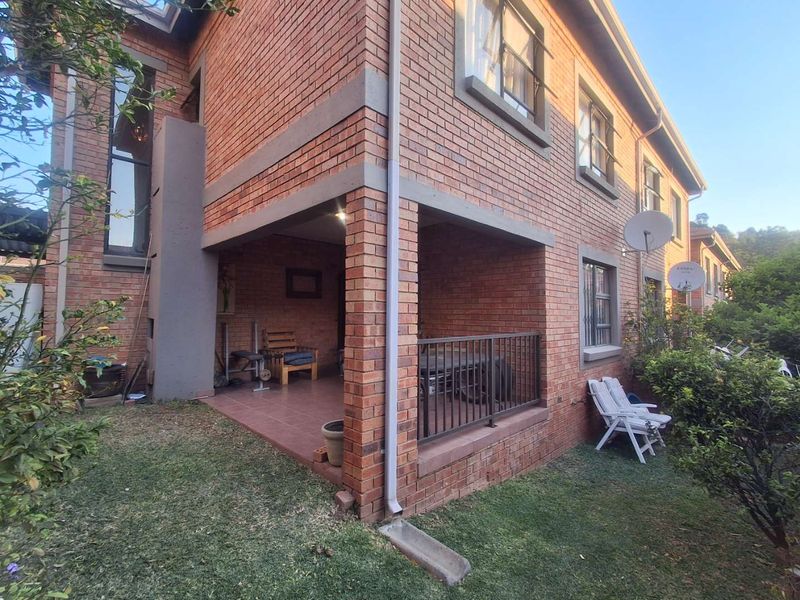 A view of the rear brick facade of the townhouse, featuring a covered patio area with tiled flooring and metal railings.