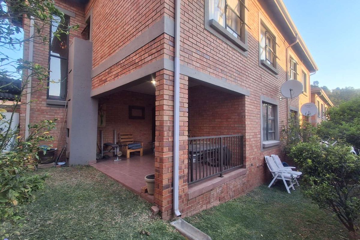 A view of the rear brick facade of the townhouse, featuring a covered patio area with tiled flooring and metal railings.