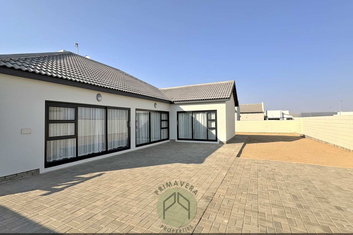 Rear view of the property featuring a spacious paved patio area, modern sliding glass doors, and a secure boundary wall.