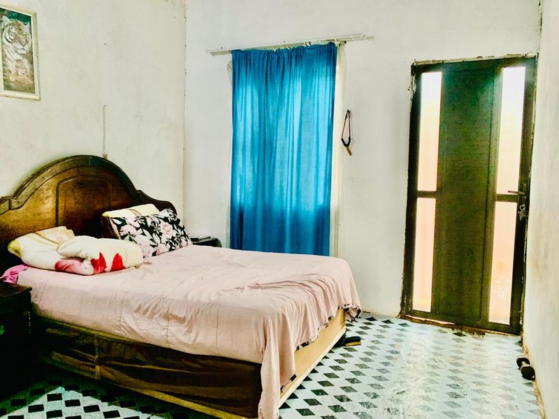 A bedroom featuring tiled flooring, a window with curtains, and a door leading to an exterior area, requiring cosmetic updates to wall and floor finishes.