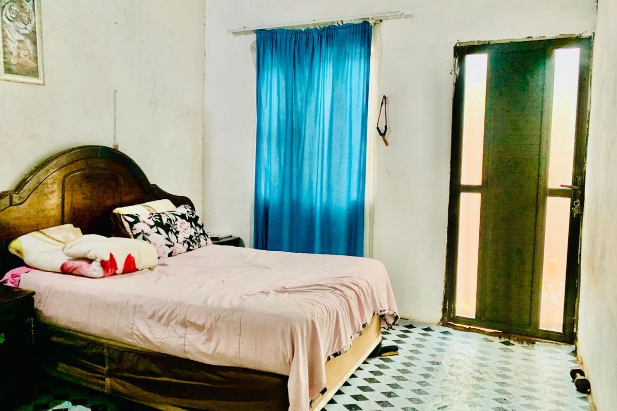 A bedroom featuring tiled flooring, a window with curtains, and a door leading to an exterior area, requiring cosmetic updates to wall and floor finishes.