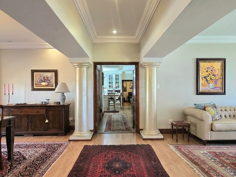 Spacious open-plan living and dining area featuring elegant decorative columns, crown molding, and polished hardwood flooring with a view into the kitchen.