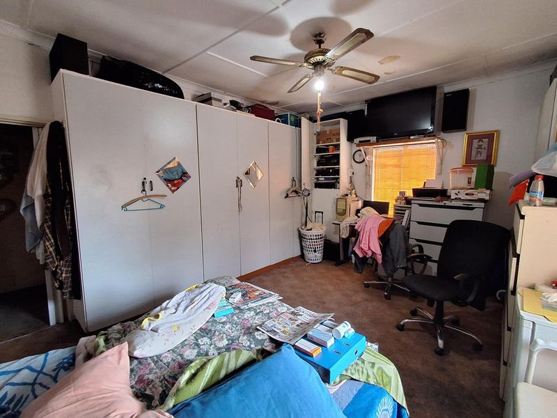 A bedroom featuring built-in cupboards, a ceiling fan, and window blinds, showing signs of wear and ceiling water damage.