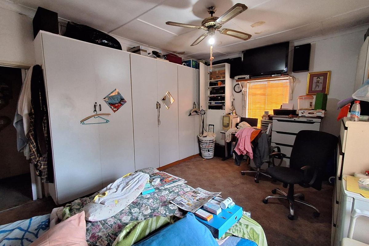 A bedroom featuring built-in cupboards, a ceiling fan, and window blinds, showing signs of wear and ceiling water damage.