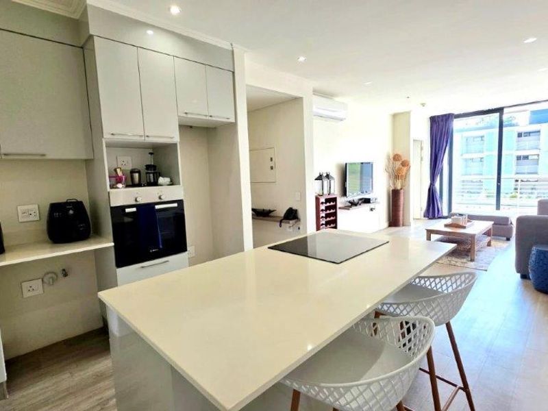 Modern open-plan kitchen and living area featuring a central island, built-in oven, sleek cabinetry, and direct access to a balcony through sliding glass doors.