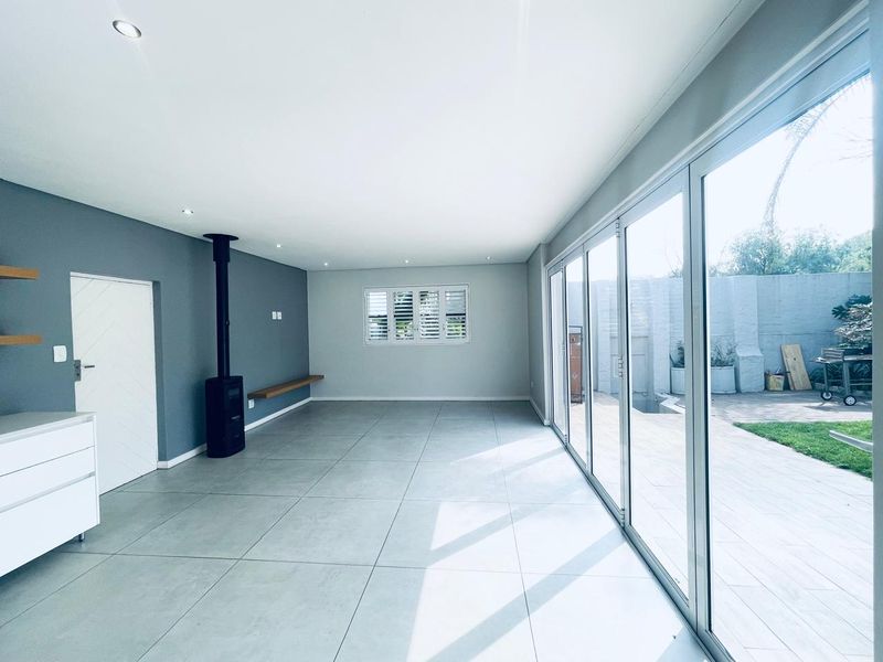 Spacious, light-filled living area featuring large sliding glass doors, tiled flooring, a modern freestanding fireplace, and plantation shutters.