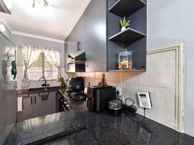 Modern kitchen featuring dark grey cabinetry, granite countertops, gas hob, extractor fan, and tiled backsplash with an integrated security alarm keypad.