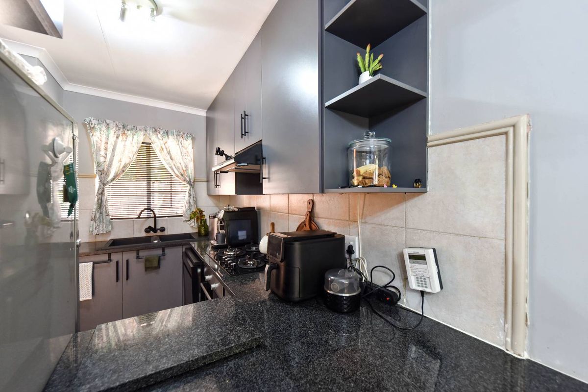 Modern kitchen featuring dark grey cabinetry, granite countertops, gas hob, extractor fan, and tiled backsplash with an integrated security alarm keypad.