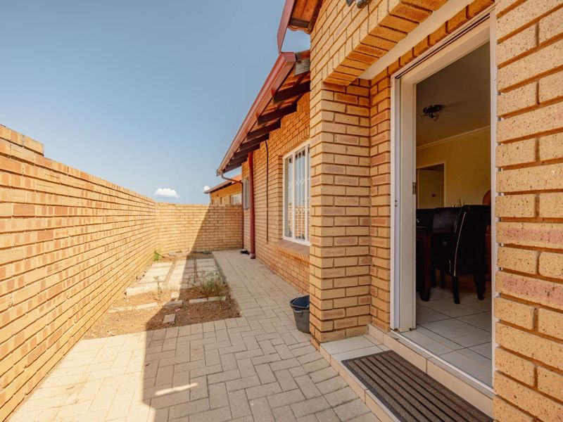 A rear exterior view of the townhouse featuring a paved patio area, face brick walls, and access to the interior living space.