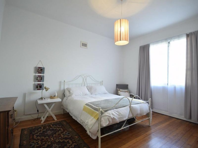 A well-lit bedroom featuring original hardwood flooring, a neutral color palette, and a large window with curtains providing natural light.